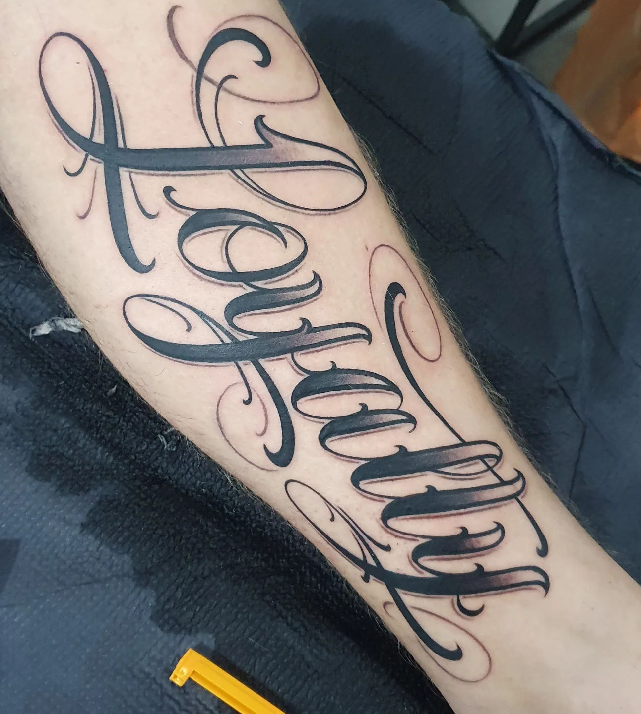 Kaligraficzny tatuaż z napisem Family na przedramieniu